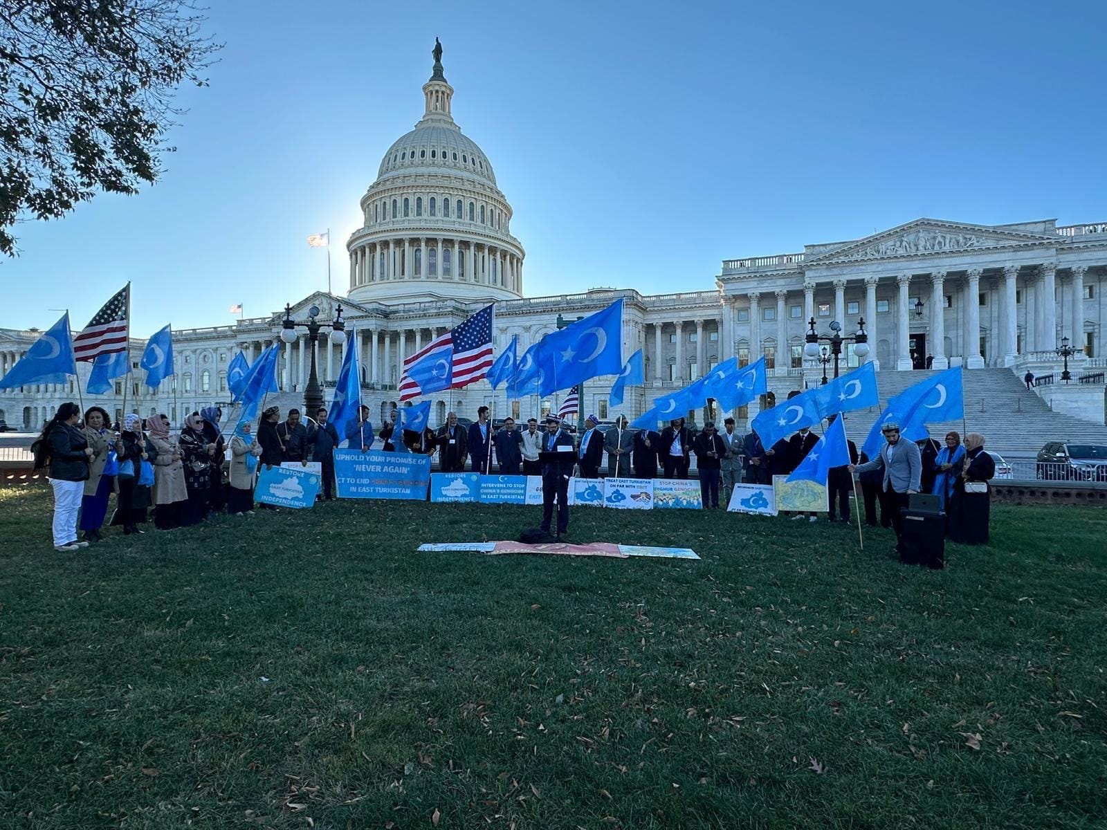 A crowd holding East Turkistan and American flags in front of the United States Capitol.