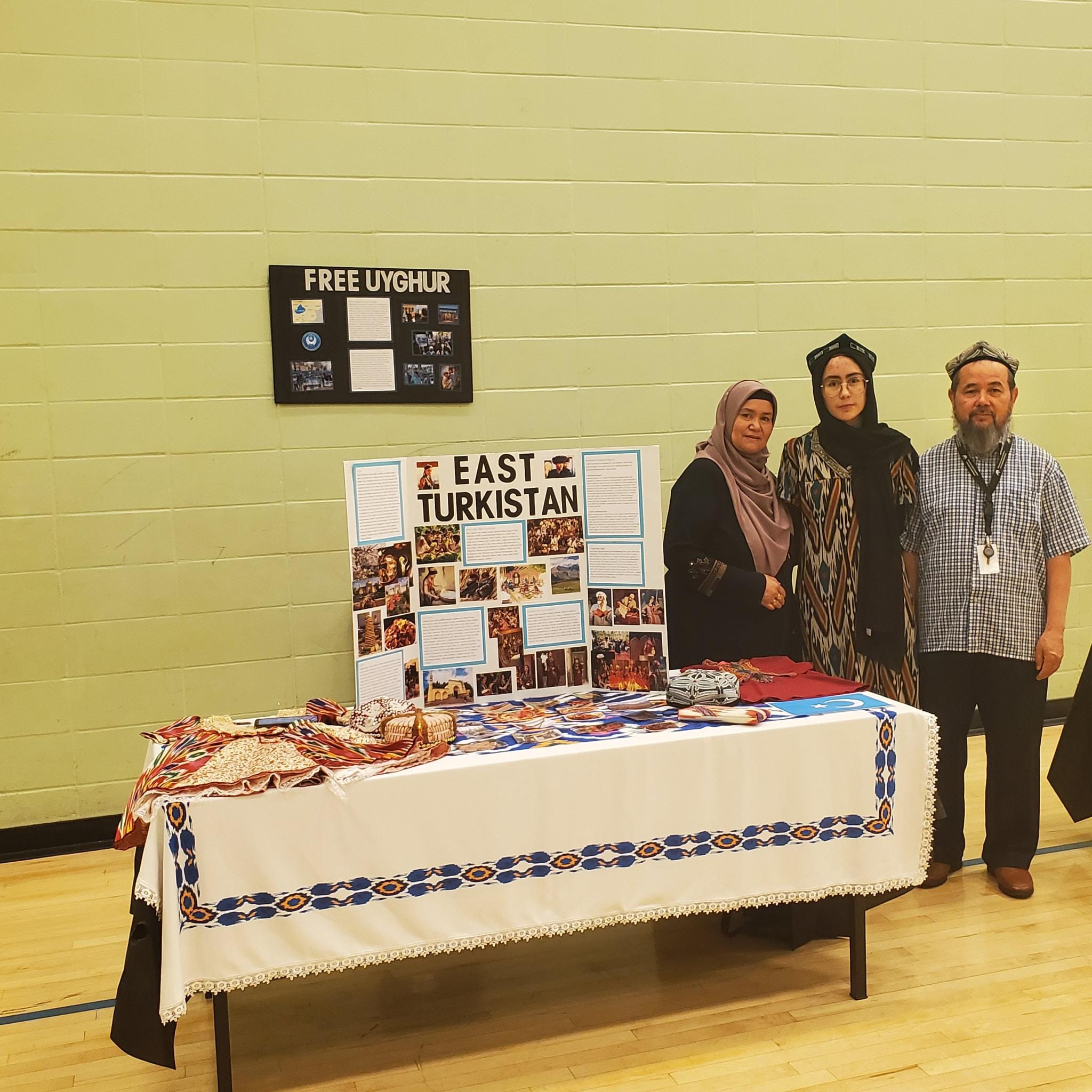 Community members beside an East Turkistan cultural display table at a local event.