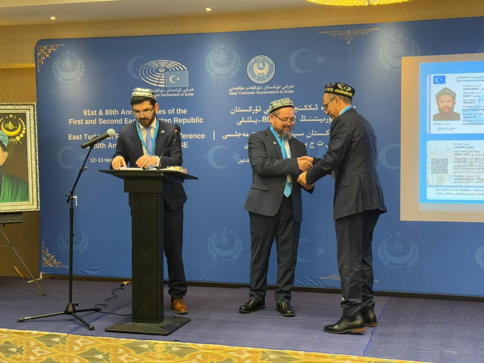 Officials shaking hands on stage at an East Turkistan Government-in-Exile ceremony.